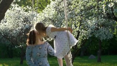 Elbise öpücüğü anne güzel kız çiçek bahçesinde salıncaklar üzerinde durmak. Yavaş çekim