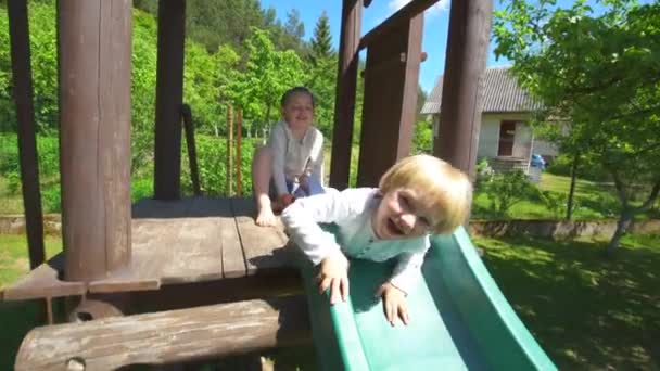 Crianças marotas deslizam para baixo no parque infantil. Rapaz e rapariga felizes brincam. Portátil — Vídeo de Stock