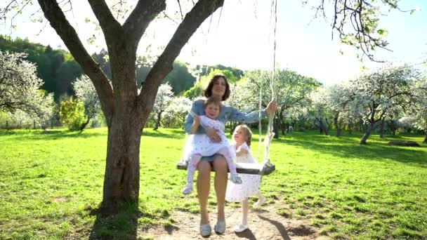 Ευτυχισμένη μητέρα που ταλαντεύεται με τις κόρες της σε κούνια στο φως του ήλιου. Στατικός πυροβολισμός. — Αρχείο Βίντεο