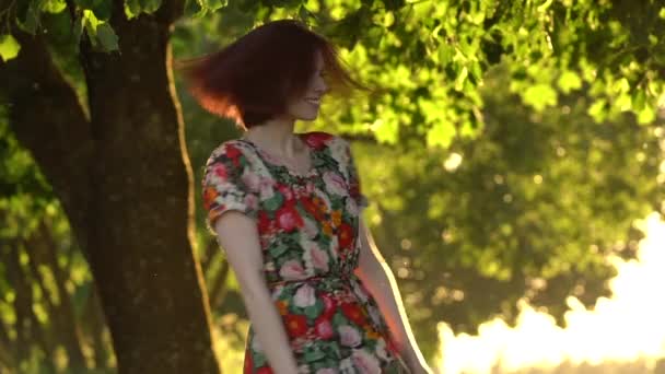 Gyönyörű vörös hajú nő spin körül a naplemente fény parkban. Lassított mozgás — Stock videók