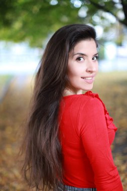 Uzun saçlı esmer, kırmızı bluzlu, gülümseyen.