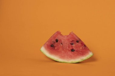 Isırılmış kırmızı karpuz dilimi turuncu arka planda