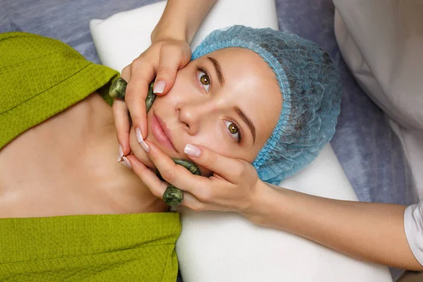 Spa treatment. Facial massage with jade stones. Alternative medicine. Massage cheeks zone. Guasha