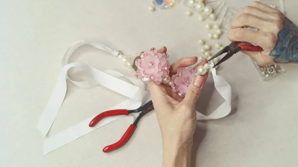 Girl fashion designer makes jewelry. Shooting close-up. She makes a ring on the decoration. Ribbons and artificial flowers are on the table