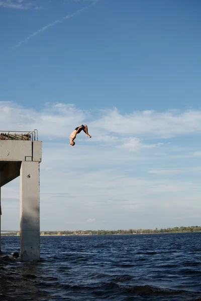A man is jumping into the sea from a high pier. Adrenaline and extreme sports. Back flip jump.