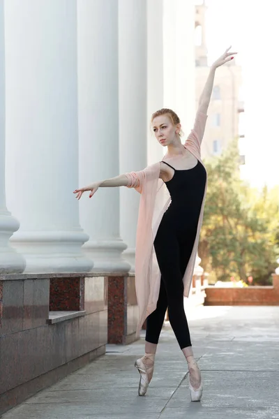 A ballet dancer in the pointe dance in the street. The girl is posing by the columns. Slender female feet. Classical ballet.