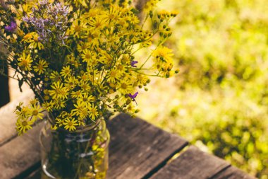 ahşap bir arka plan üzerinde cam bir kavanozda sarı kır çiçekleri buket