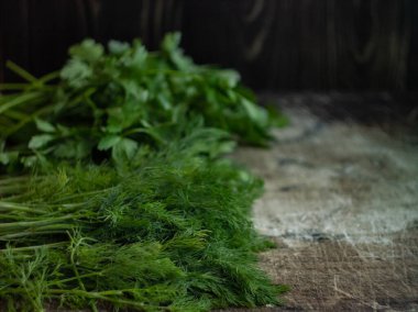 Koyu, eski bir ahşap arka planda yeşil baharatlı dereotu ve maydanoz, çözünmüş fotoğraf, bulanık arkaplan; koyu bir arka planda yeşil çimenlerin soyut kompozisyonu, ev tariflerinde pişirme