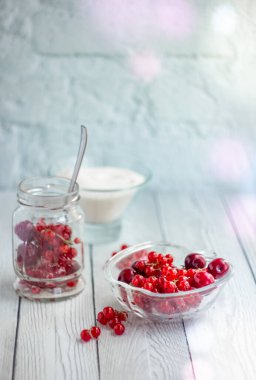 Cam bir kavanozda üzümler ve kirazlar, beyaz bir masanın arka planında böğürtlen ve şeker dolu bir cam tabak; yaz reçel tarifleri için hafif arka plan