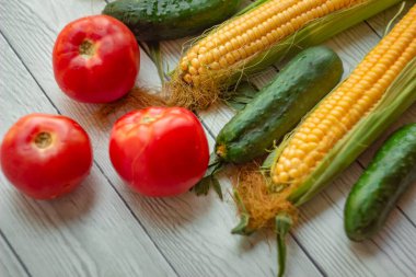 Olgun mısır, kırmızı domates ve taze salatalıklar hafif bir ahşap masa üzerinde uzanır; sebze buketi, hasat