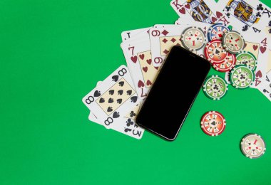 yeşil bir masada iskambil kartları ile cep telefonu ve poker fişleri