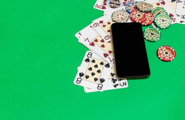 yeşil bir masada iskambil kartları ile cep telefonu ve poker fişleri