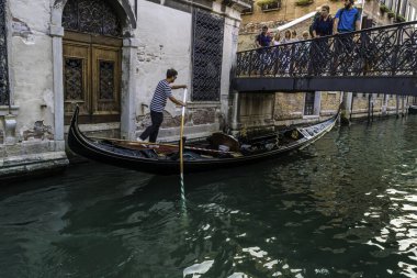 Gondolcu gondolunu çekiyor ve İtalya, Venedik 'te alçak bir köprünün altından geçmeye hazırlanıyor.