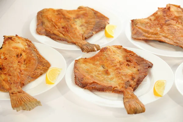 Fried flat fish on white plates and lemons