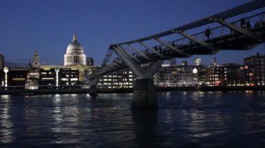 Londra, İngiltere 'de Thames nehri boyunca uzanan St. Pauls Katedrali ve Milenyum Köprüsü görüntüsü nehir dalgalanmaları ve köprüde yürüyen insanların görüntüsü Londra' nın manzarasında popüler turizm ve turizm simgeleridir.