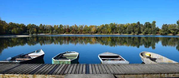 Herbstlandschaft mit See, Bootsbrücke und einigen Booten. — Stockfoto