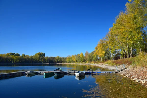 Herbstlandschaft mit See, Bootsbrücke und einigen Booten. — Stockfoto