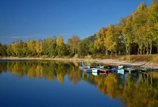 Herbstlandschaft mit See, Bootsbrücke und einigen Booten. — Stockfoto