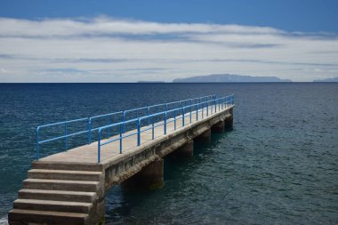 Merdiveni ve okyanusta mavi tırabzanı olan küçük bir iskele. Santa Cruz, Madeira, Portekiz. Arkaplanda adalar.