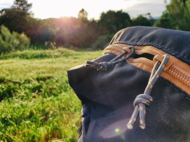 cremalleras de mochila con la hierba, el bosque y el atardecer de fondo