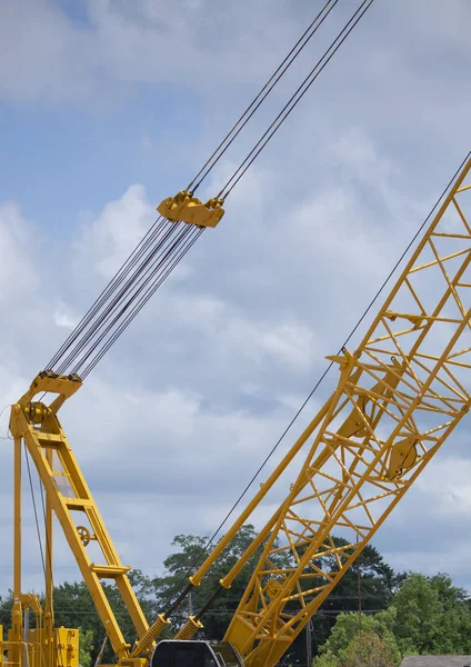 Yellow and black construction crane arm and cables against a cloudy sky