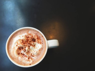 Kahve, sabah kafedeki siyah masanın üzerinde beyaz bir bardakta. Nesnelere odaklanma. Sıcak ton.