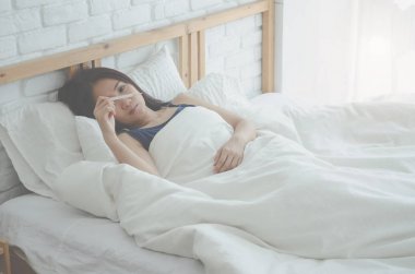 Asyalı kız gri pijama ve şort uyuyor. Beyaz yatak odasında yatakta. Güneş ışığına neden olan genç bir kızın yüzündeki karanlık lekeler. Pamuk ve güneşli.