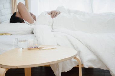 Asyalı erkekler hasta Sabah odada beyaz yatakta yalan. Yatak odasında uyuyan bir adam vardı. Sıcak bir ton. Nesnelere odaklanma.