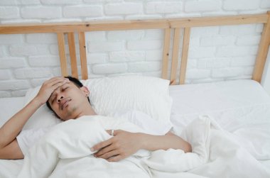 Asyalı erkekler hasta Sabah odada beyaz yatakta yalan. Yatak odasında uyuyan bir adam vardı. Sıcak bir ton. Nesnelere odaklanma.