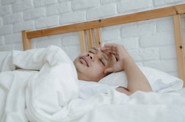 Asyalı erkekler hasta Sabah odada beyaz yatakta yalan. Yatak odasında uyuyan bir adam vardı. Sıcak bir ton. Nesnelere odaklanma.