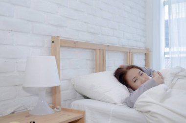 Beyaz odadaki yatakta. Yatak odasında uyuyan güzel bir kadın. Asyalı kız iyi. Elleri alnında, kadınlar. Sıcak ton.