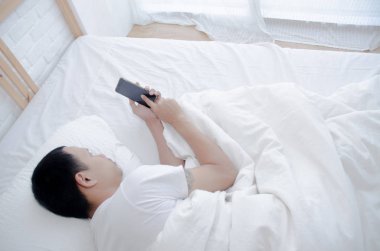 Asyalı adam odada yatakta smasphone oynar. Sabah yatak odasında dinleniyordu..