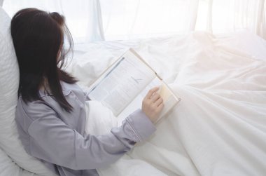 Sabah beyaz oda kadınlar okuyor. Bayan mutlu okumuş. Beyaz yatakta bilgi için eğitim gören kadınlar vardır. Sıcak ton. Nesnelere odaklanmayın.