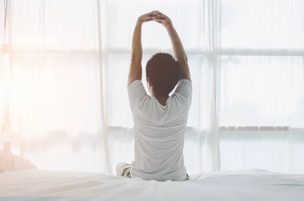 Men wear white and black striped shirts at the edge of the bed. To relax in the morning after waking up Men sit at the edge of the bed.And stretching his arms to relax in the morning.