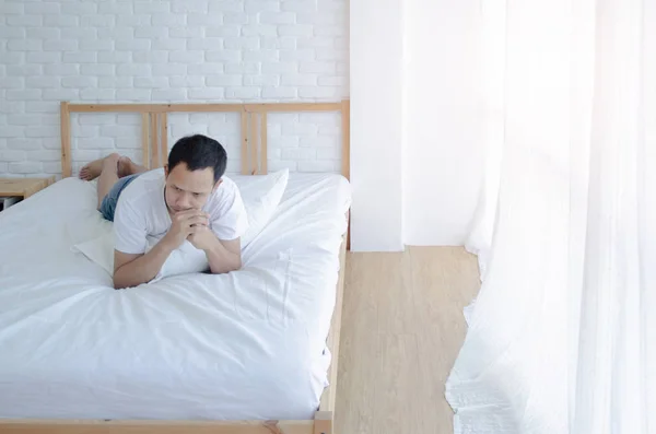 Men are sitting at the edge of the bed in the room and have stress.Young man wearing a white shirt with both hands on his head. Because of pain.