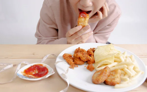 亚洲女孩穿着粉红色的衬衫在桌子上吃垃圾食品 白盘油炸食品 腰围在桌子上 健康饮食和积极的生活方式 不要聚焦于对象 — 图库照片