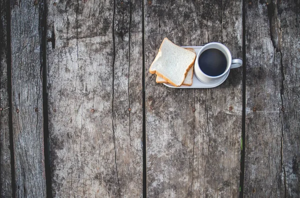 Black coffee and bread plate on wooden table.White bread and glass placed on the table in the morning.On the breakfast table there was a glass of coffee and a plate of bread.Breakfast set on wooden floor in the morning.