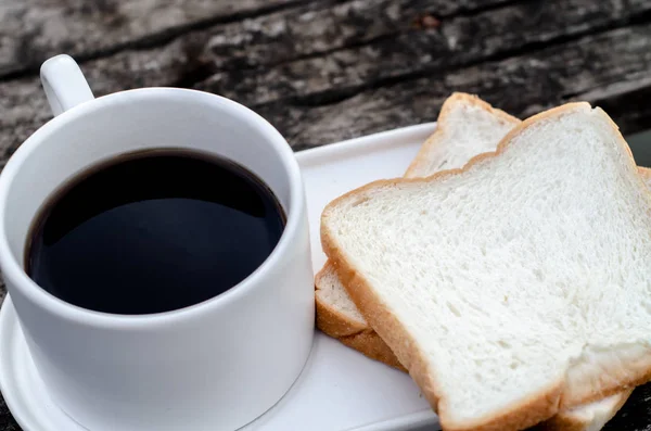 白いパンとグラスをテーブルの上に置きました 朝食テーブルの上にはグラス1杯のコーヒーとパンの盛り合わせがありました 朝はウッドフロアの朝食 — ストック写真