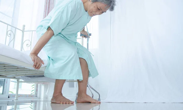 Asian elderly Wearing a green shirt Got out of bed in the nursing room.Elderly women caught the wood to help walk.