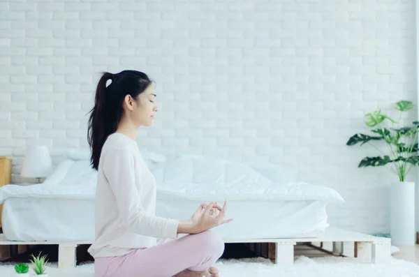 在一个温暖的早晨 坐在瑜伽上的亚洲女孩在床上摆姿势 温暖的语气 不要聚焦于对象 免版税图库图片