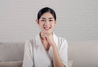 Beyaz tişörtlü, gülümseyen Asyalı kadın. Kanepede oturan kız..