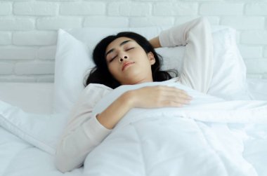 Yatak odasında uyuyan güzel bir kadın. Yüzükoyun yatağa uzanan bir kadın. Sabahları beyaz bir odada pijama giyen bir kız..