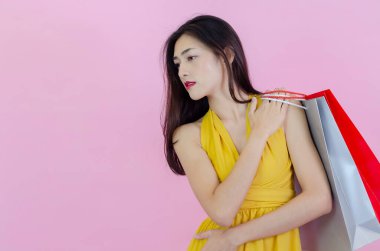 Asyalı kadınlar siyah kıyafetler giyer. Yeşil, gri, kırmızı, pembe arka planlı bir alışveriş çantası taşıyordu.