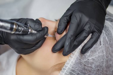 Genç bir kıza uygulanan kalıcı göz kalemi prosedürü. Yakın plan. Genç ve güzel bir kadın kozmetoloji salonunda kalıcı makyaj yapıyor. Genç bir kız güzellik salonuna sürekli göz kalemi sürüyor.