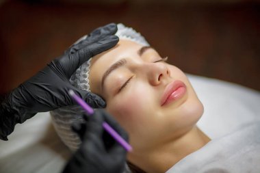 Genç bir kıza uygulanan kalıcı göz kalemi prosedürü. Yakın plan. Genç ve güzel bir kadın kozmetoloji salonunda kalıcı makyaj yapıyor. Genç bir kız güzellik salonuna sürekli göz kalemi sürüyor.