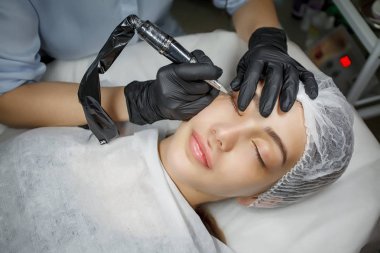 Genç bir kıza uygulanan kalıcı göz kalemi prosedürü. Yakın plan. Genç ve güzel bir kadın kozmetoloji salonunda kalıcı makyaj yapıyor. Genç bir kız güzellik salonuna sürekli göz kalemi sürüyor.