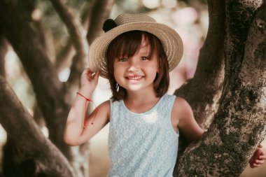 Bir şapka ve beyaz elbise güzel bir küçük kız güzel bir sonbahar sıcak gününde bir ağacın yanında duruyor. Beyaz elbise giymiş sevimli küçük kız açık hava portresi.