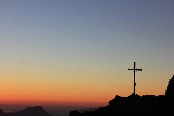 素晴らしい赤い色の空と頂上の十字架とスイスの山々のカラフルな夕日 ストックフォト