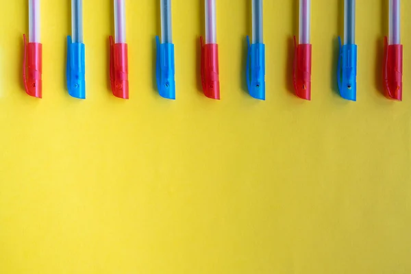 Bolígrafos mixtos azules y rojos sobre un fondo amarillo desde arriba. Colocación plana, espacio para copiar, vista superior . —  Fotos de Stock