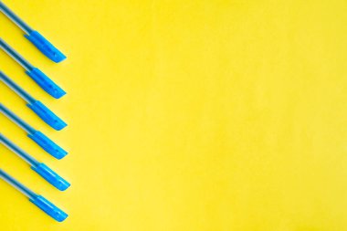 Sol taraftaki sarı arka planda mavi tükenmez kalemler. Düz konum, boşluk kopyala, üst görünüm.